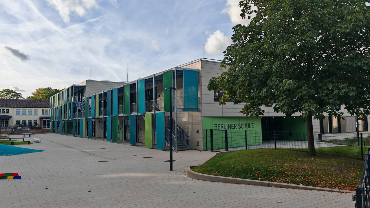 Neubau der Berliner Schule Korbach mit grünen und blauen Fassadenpaneelen, Laubengängen, Außentreppe und Schulhof