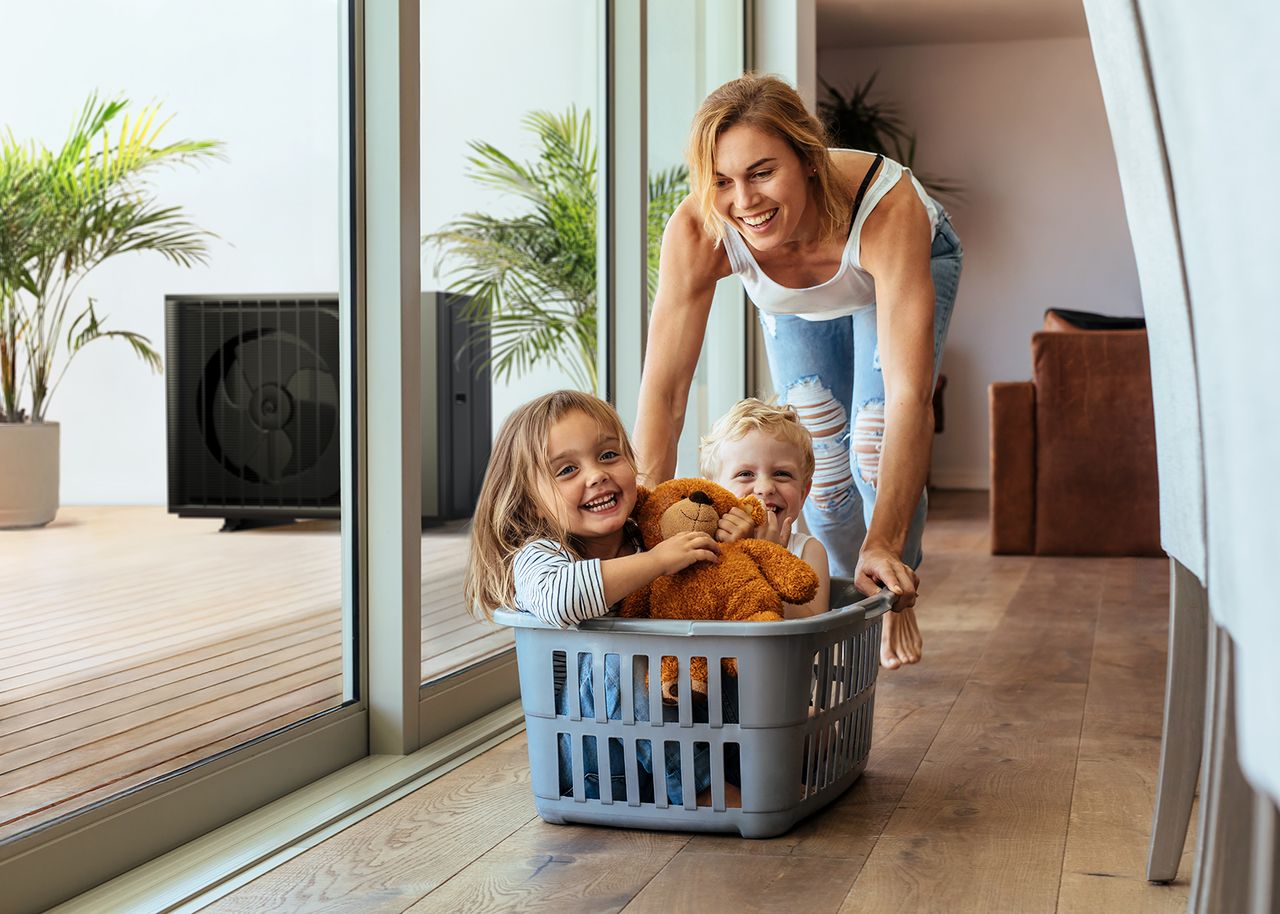 Mutter schiebt zwei Kinder in Wäschekorb über den Fußboden