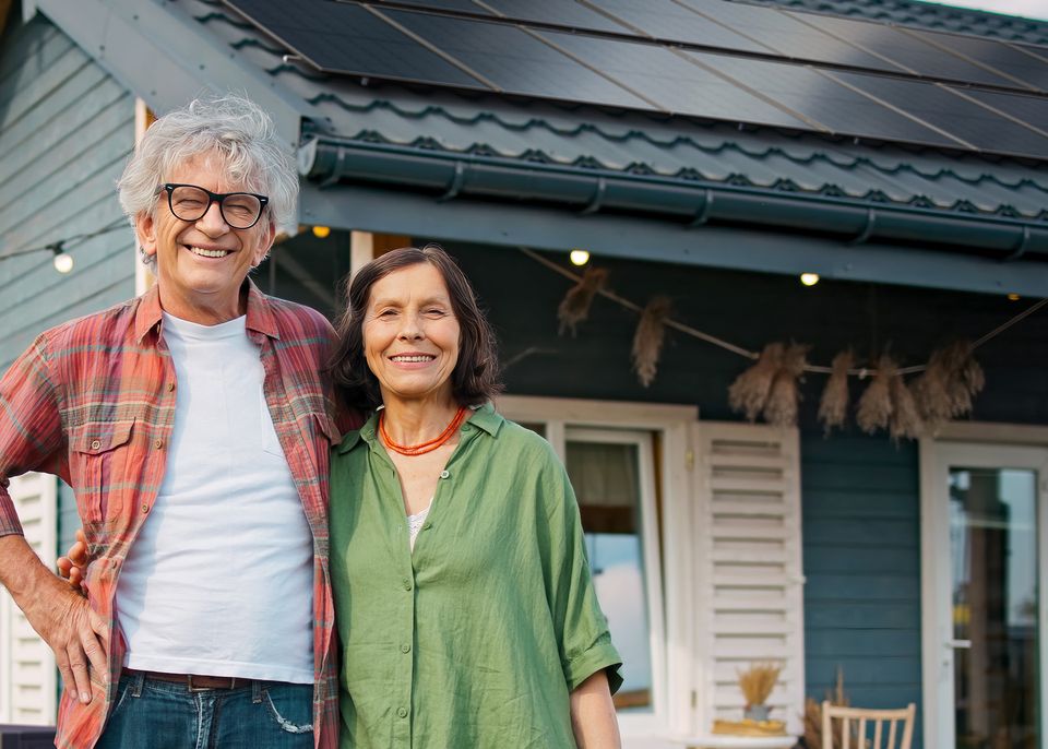 Älteres Ehepaar steht lächelnd vor einem Haus mit PV-Anlage