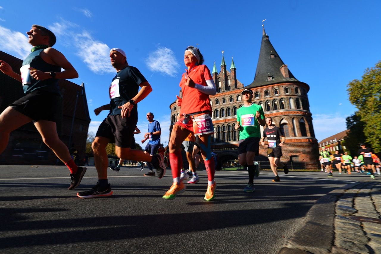 Runners participating in a marathon pass by a historic brick building with towers under a clear blue sky.