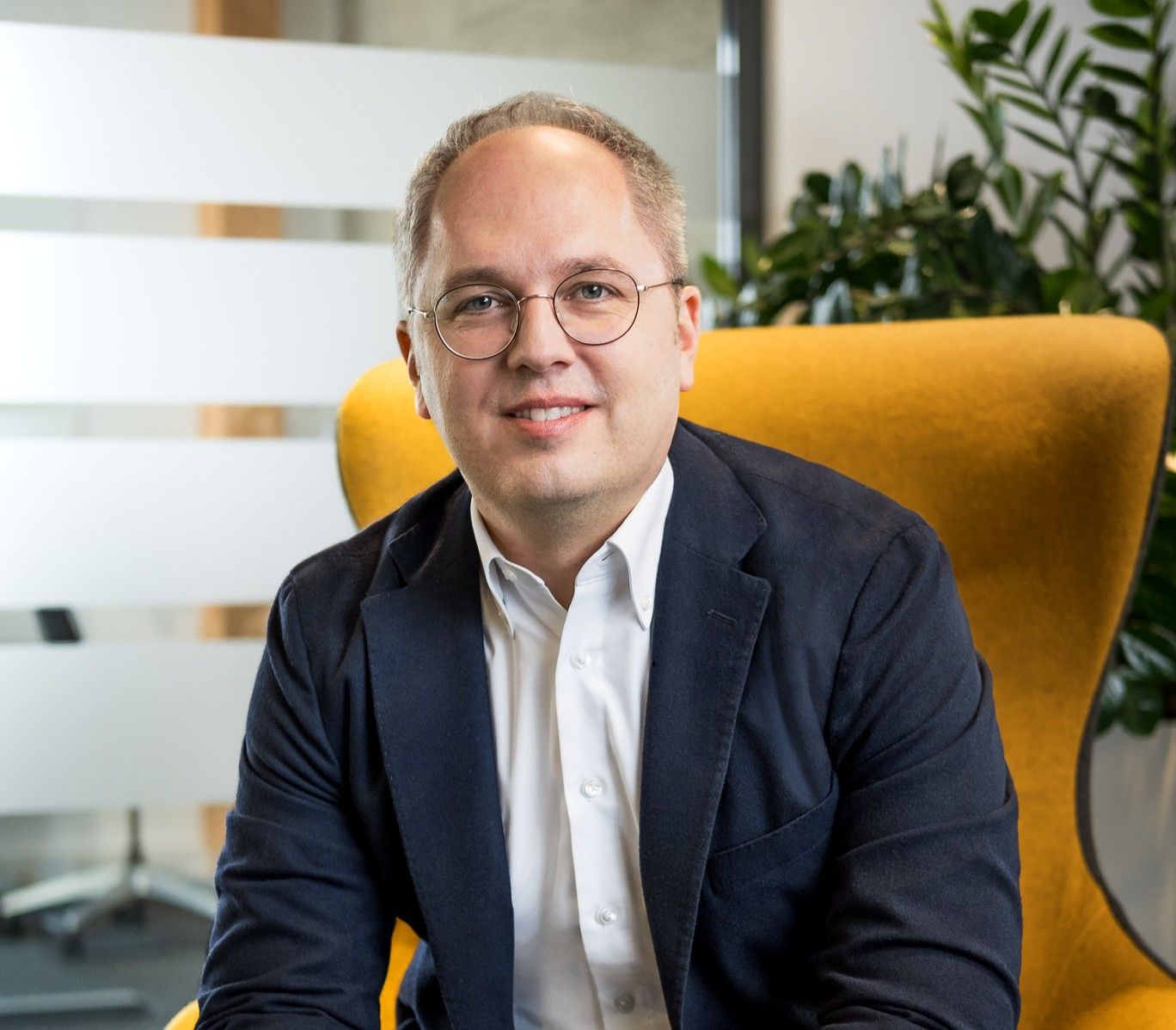 CEO Jens Meier sitzt auf einem gelben Sessel und lächelt in die Kamera