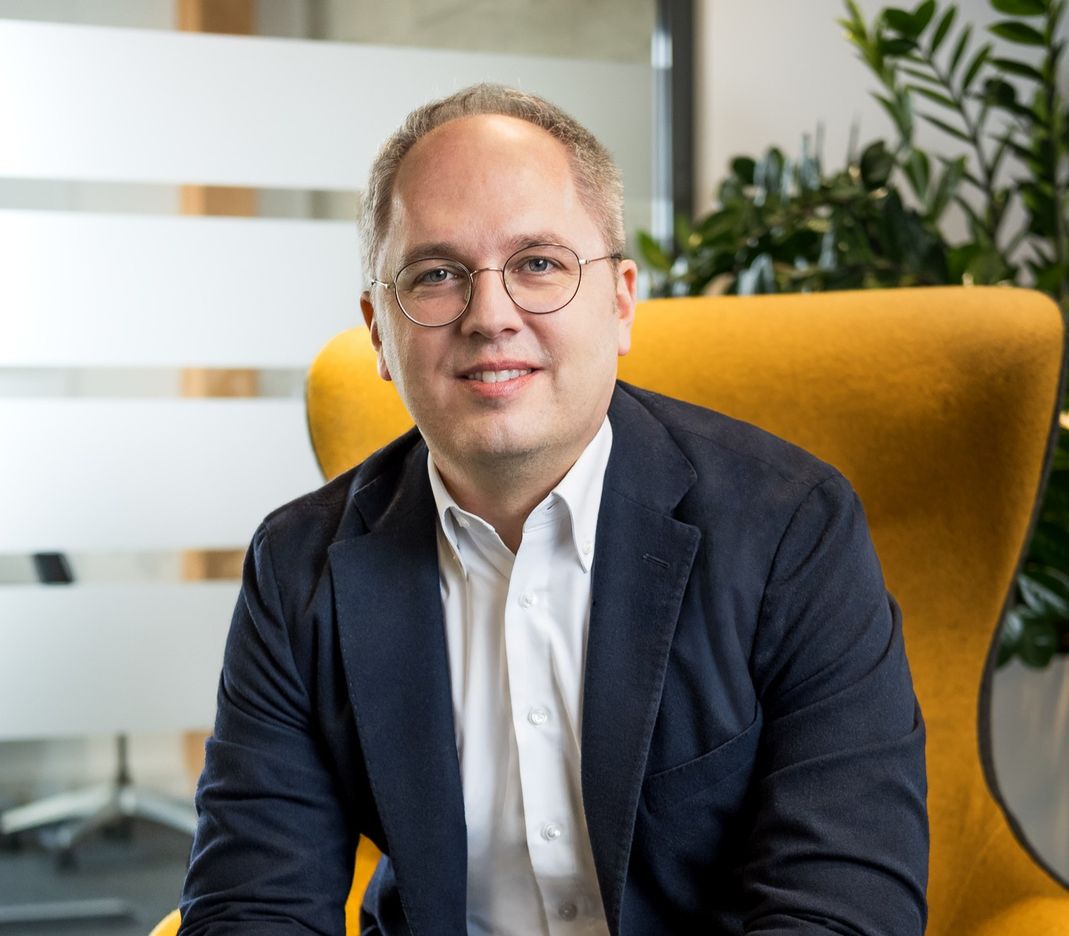 CEO Jens Meier sitzt auf einem gelben Sessel und lächelt in die Kamera