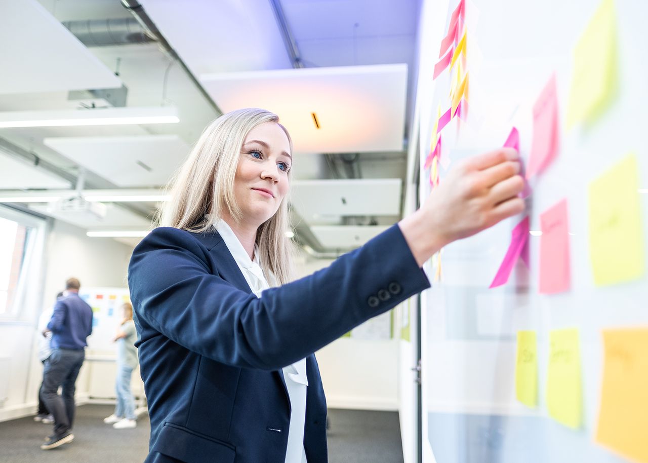 Frau steht vor White Board und klebt ein Post-it fest