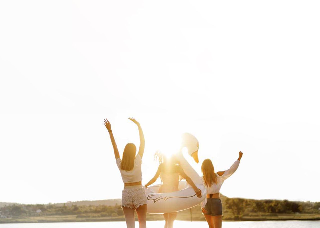 Drei Frauen mit Sommerkleidung und Schwimmring vor einem See