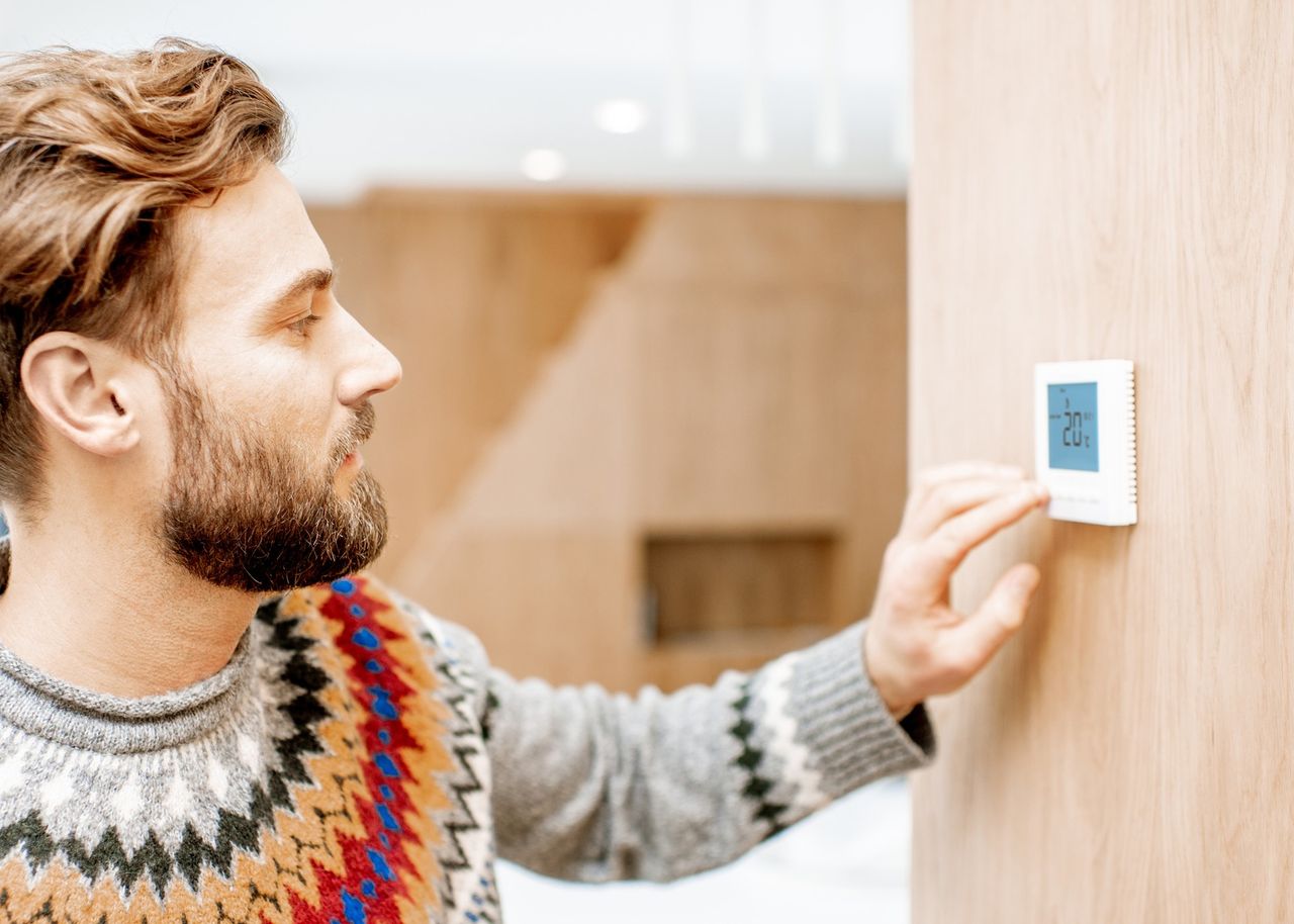 Mann stellt die Temperatur mit dem Thermostat zu Hause ein