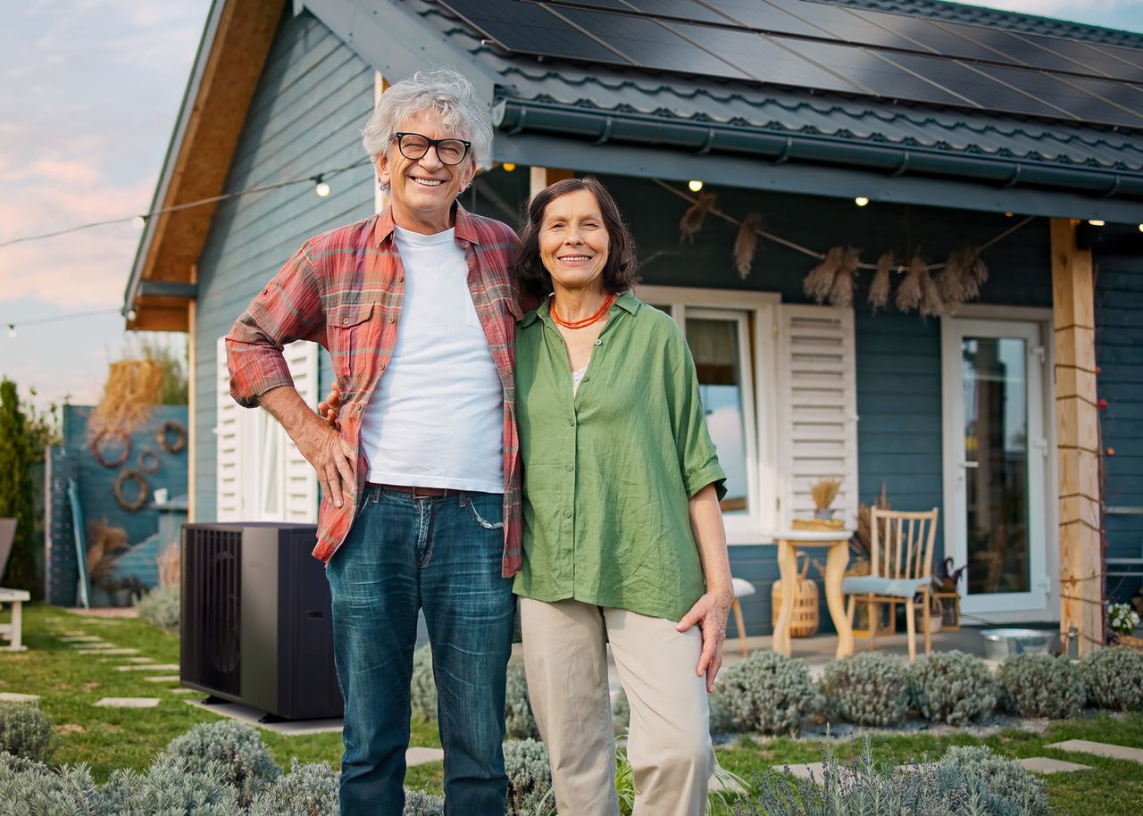 Älteres Ehepaar steht glücklich vor einem Haus mit PV-Anlage