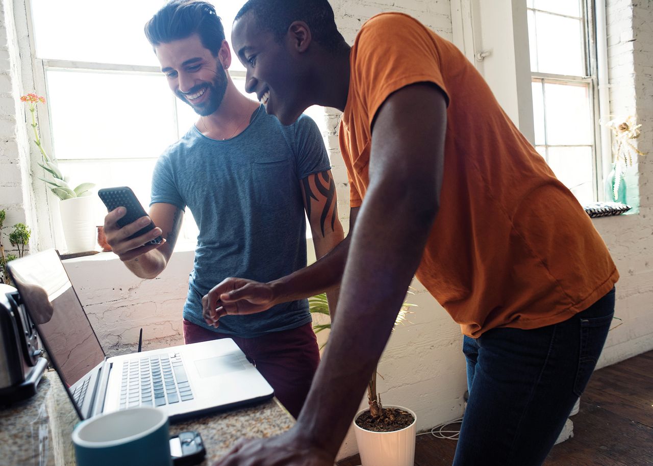 Zwei Männer gucken auf Smartphone und Laptop