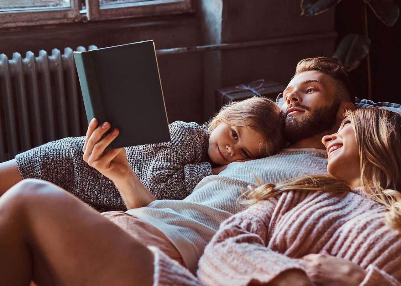 Familie kuschelt auf Sofa und ließt ein Buch.