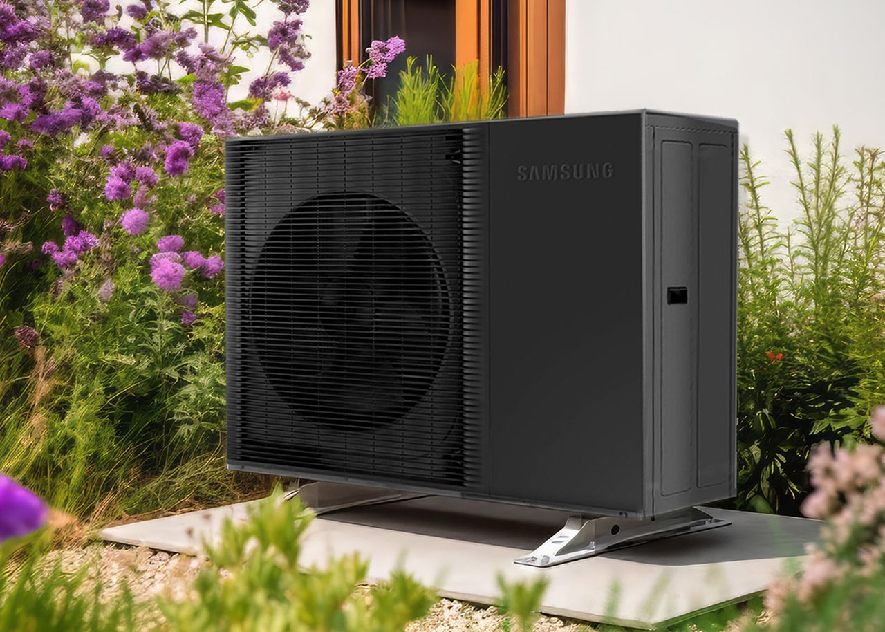 Wärmepumpe vor Haus, umgeben von Blumen