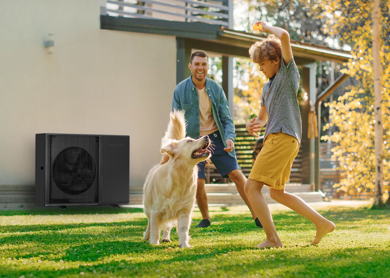 Vater und Sohne spielen mit Hund vor Haus mit Wärmepumpe