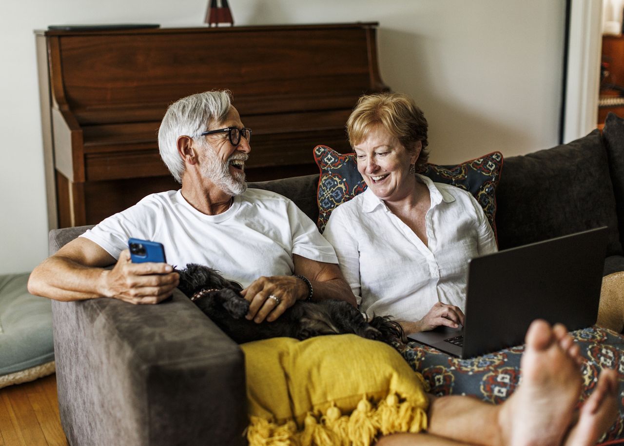 Mann und Frau sitzen auf dem Sofa mit Handy und Laptop