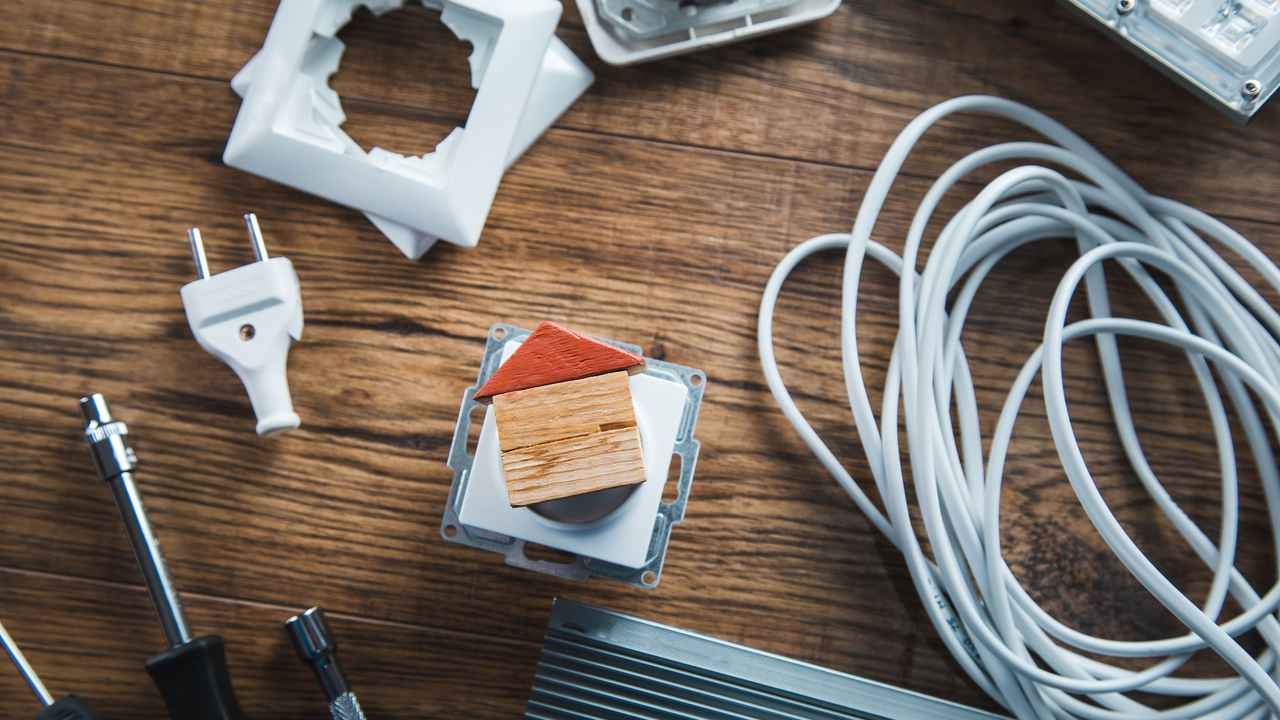 Assorted electrical tools and components, including a plug, screwdriver, and coiled cable, arranged on a wooden surface.