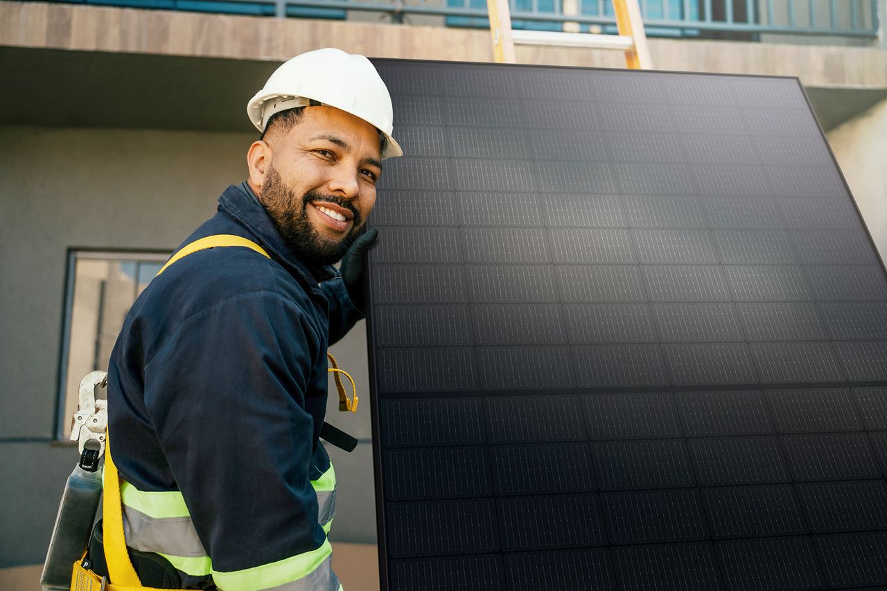 Arbeiter mit Helm und Schutzkleidung vor einem PV-Panel