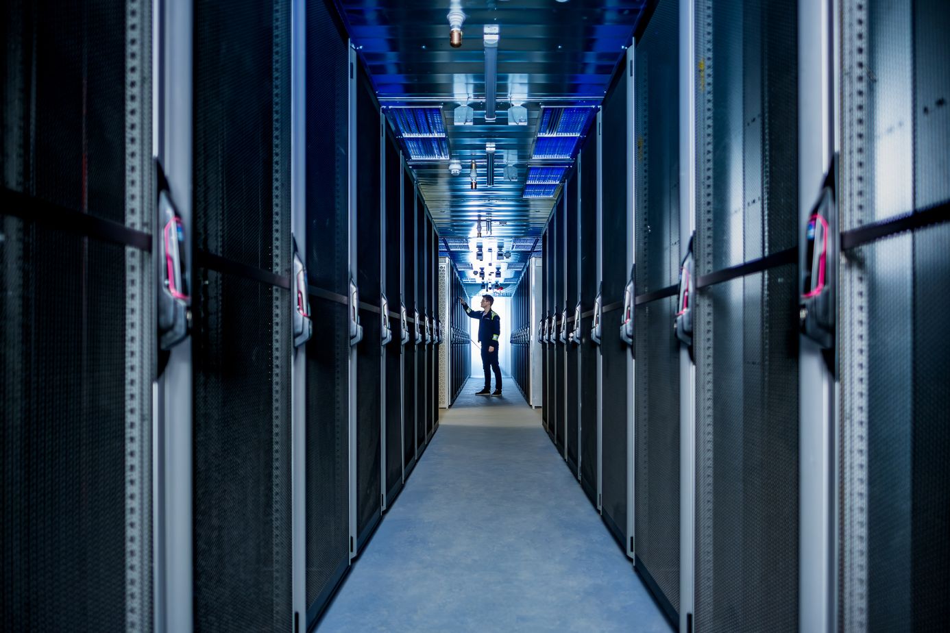 Eine Person arbeitet in einem schmalen Gang zwischen Reihen von Server-Racks in einem hell erleuchteten Rechenzentrum.