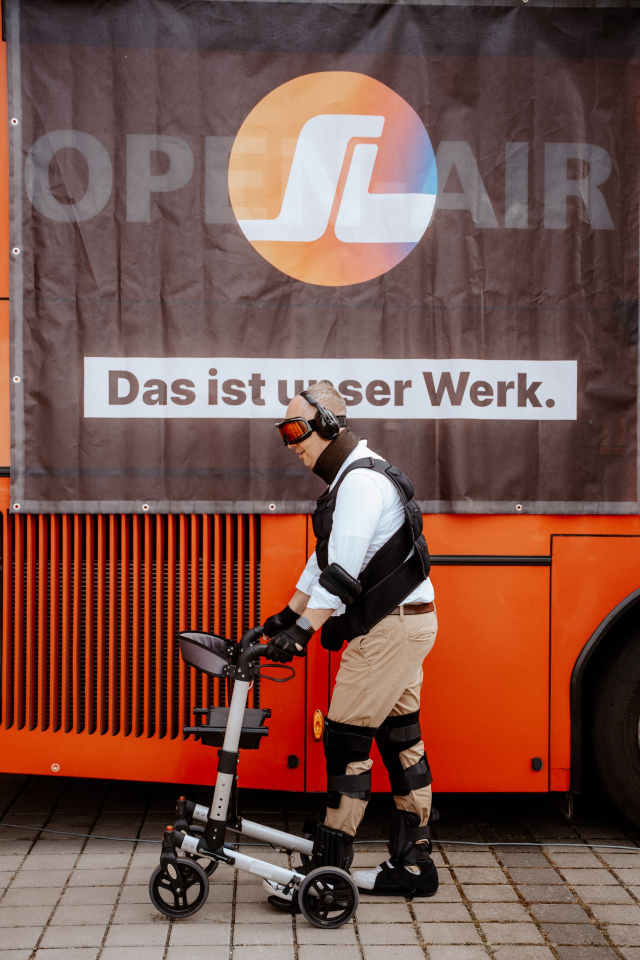 Jens Meier trägt einen Alterssimulationsanzug mit Gehwagen vor einem SWL Bus