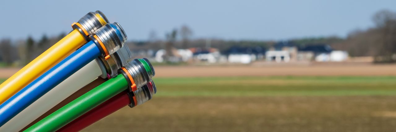 Close-up of colorful cables with metal connectors against a blurred rural landscape, featuring fields and distant buildings.