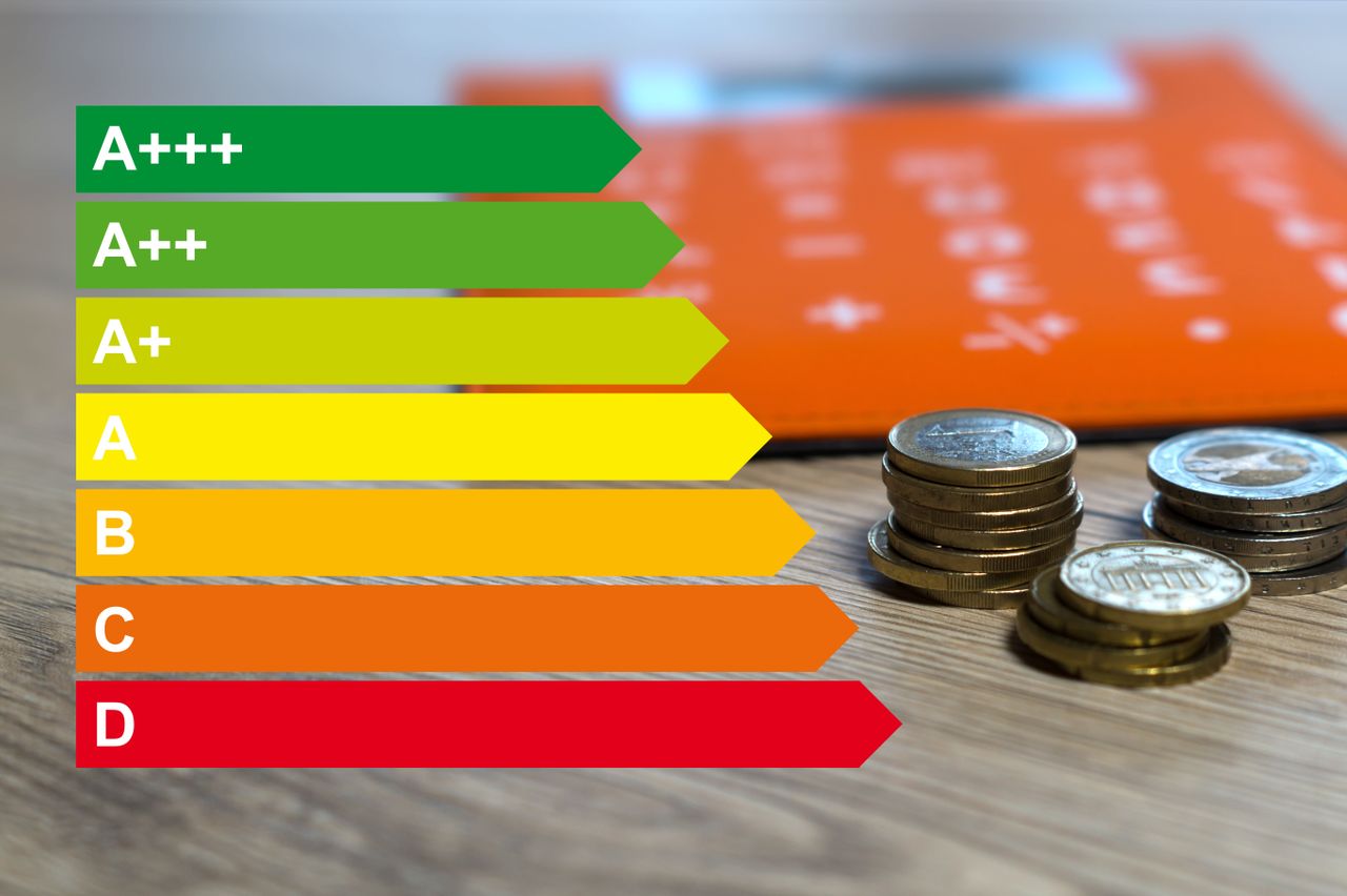 Energy efficiency rating chart from A+++ to D with stacked coins on a wooden surface, and an orange blurred background.