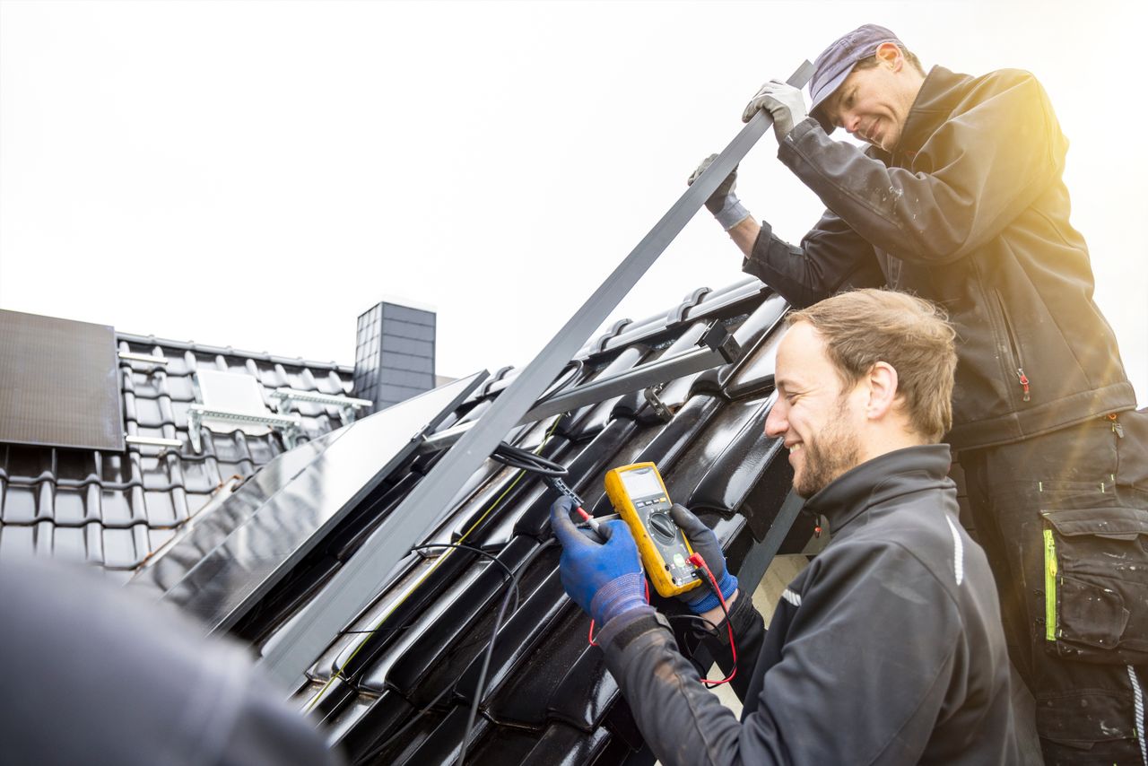 Zwei Techniker installieren PV-Anlagen auf einem schwarzen Dach