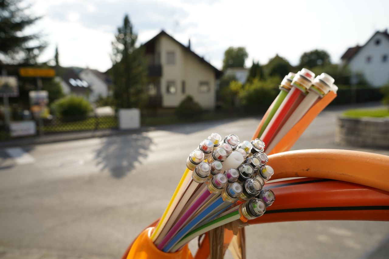 Close-up of colorful fiber optic cables bundled together, with a residential street and houses blurred in the background.