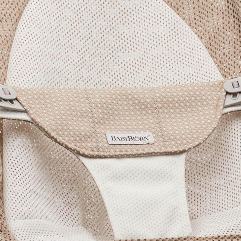 Close-up of a beige and white BabyBjörn mesh fabric with a small pocket and brand label, featuring adjustable plastic clips.
