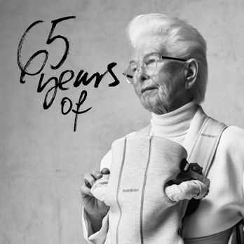 Black and white photo of an elderly person holding a baby in a carrier. Text reads "65 years of."