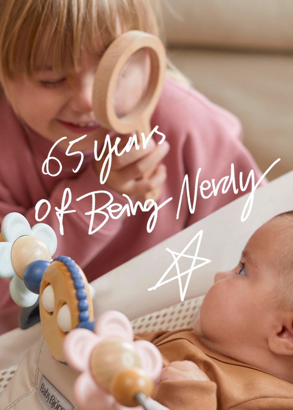 Child smiling through a wooden magnifying glass at a baby in a crib; text reads "65 years of being Nevaly" with a doodled star.