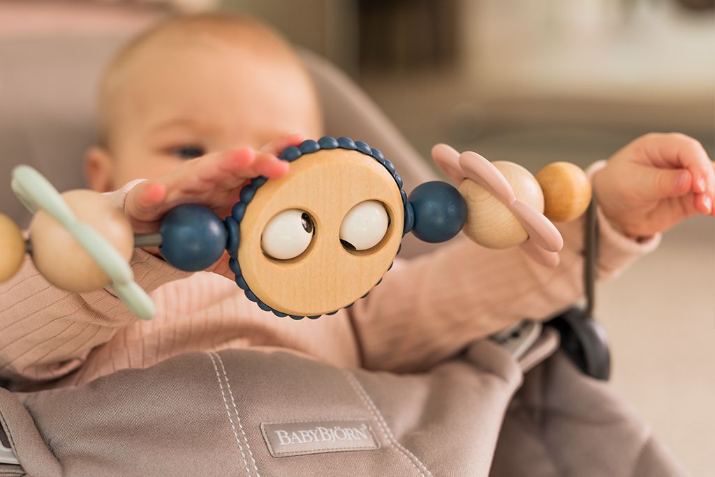 Baby in a stroller reaching for a wooden toy with colorful beads and rings.