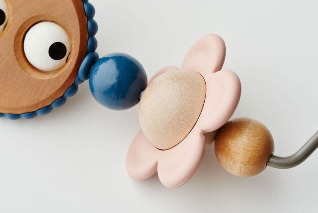 Close-up of a wooden toy featuring a blue bead, a pink flower-shaped piece, and a wooden bead, connected on a metal wire.