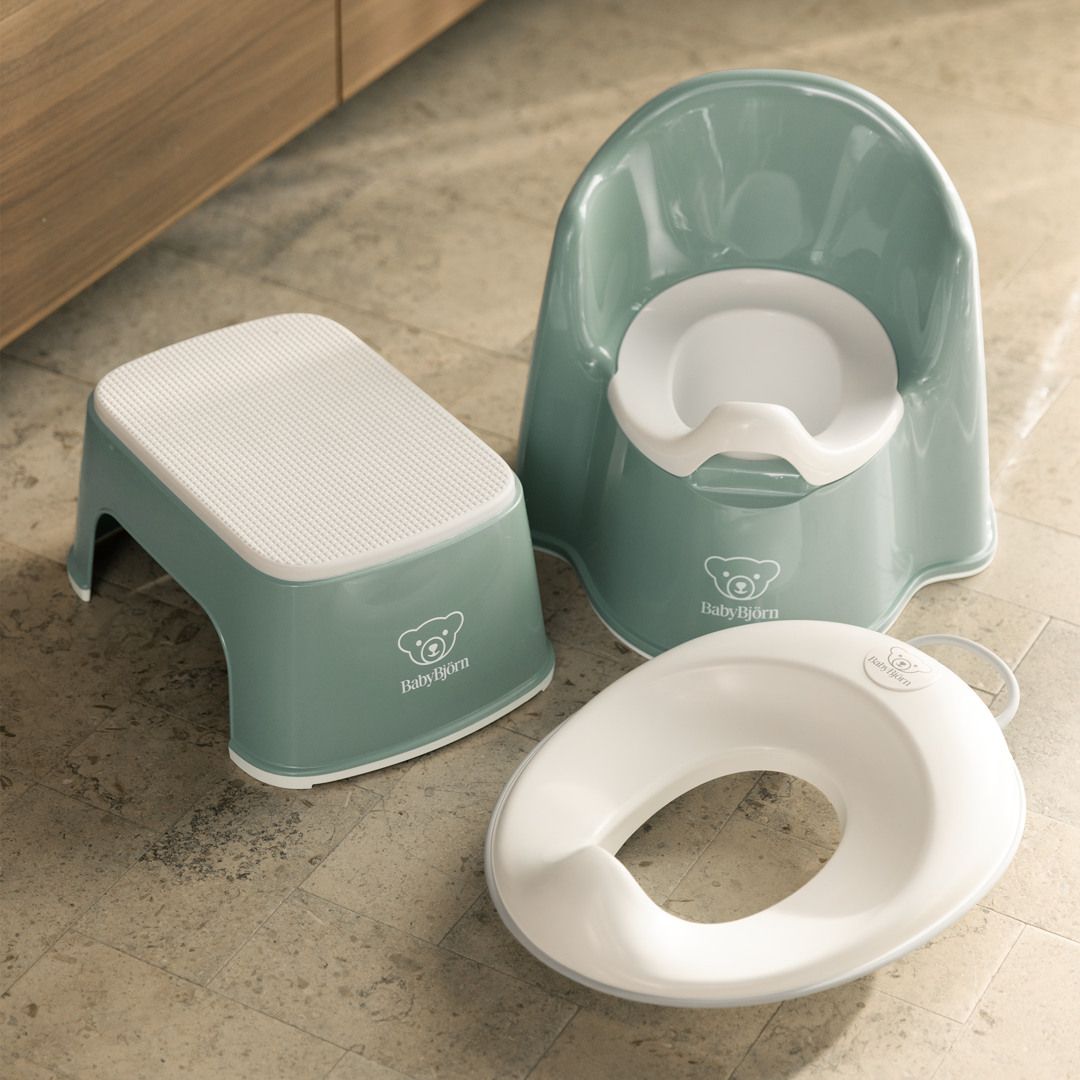 Green and white children's potty training set on a tiled floor, including a potty chair, step stool, and toilet seat adapter.
