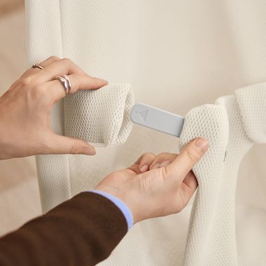 Hands adjusting a white mesh fabric strap with a gray plastic clip, showing a securing or assembly process.