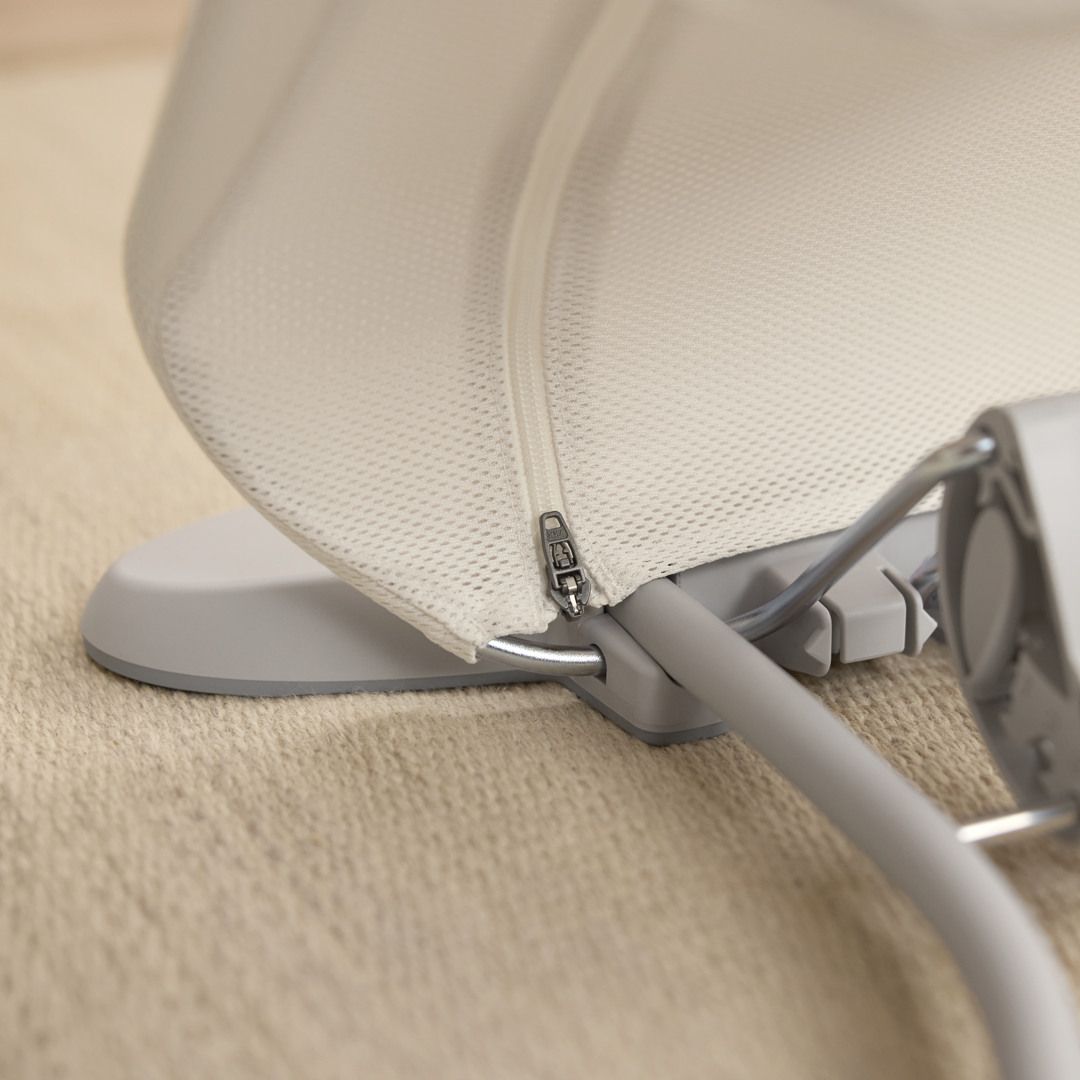 Close-up of a beige fabric canopy with a visible zipper and a metal frame, resting on a textured light brown surface.