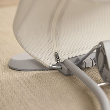 Close-up of a beige fabric canopy with a visible zipper and a metal frame, resting on a textured light brown surface.