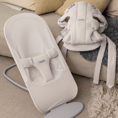 Cream-white baby bouncer and carrier seat on a beige couch with a textured rug nearby.