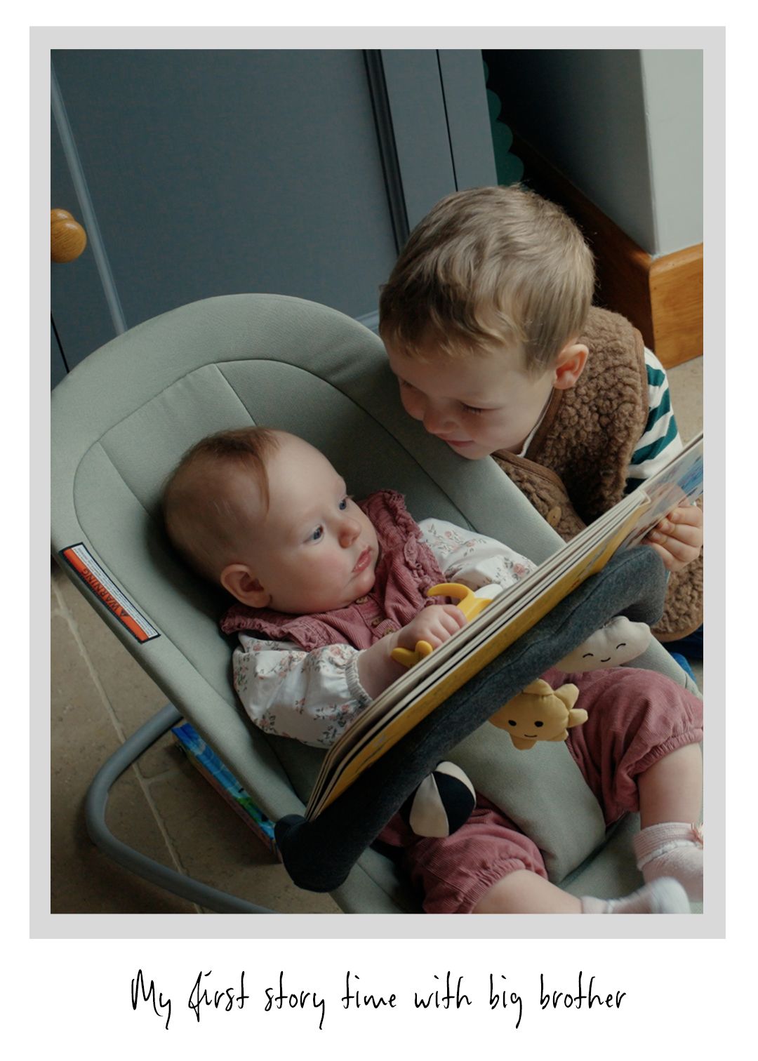 A young child reads a book to a baby in a bouncer, with a plush toy and soft lighting creating a warm, cozy atmosphere.