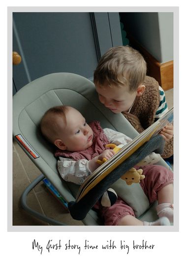 A young child reads a book to a baby in a bouncer, with a plush toy and soft lighting creating a warm, cozy atmosphere.