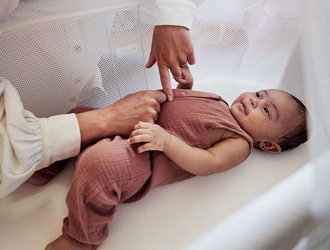 A baby in a pink outfit lies on a soft surface, while an adult gently touches its chest, creating a nurturing and tender moment.