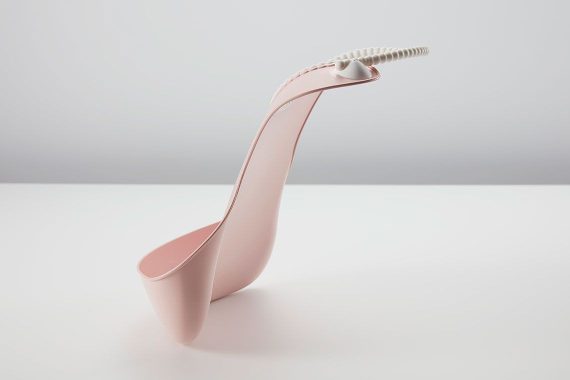 A modern, minimalist pink chair with a curved design and a coiled wire accent on a white surface against a light gray background.