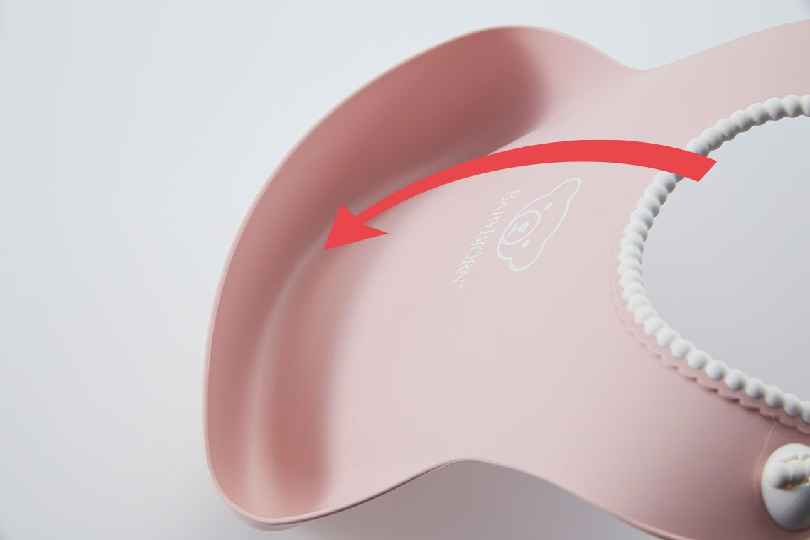 Close-up of a pink silicone bib with a curved pocket and a red arrow pointing to it. The bib has a textured strap for fastening.