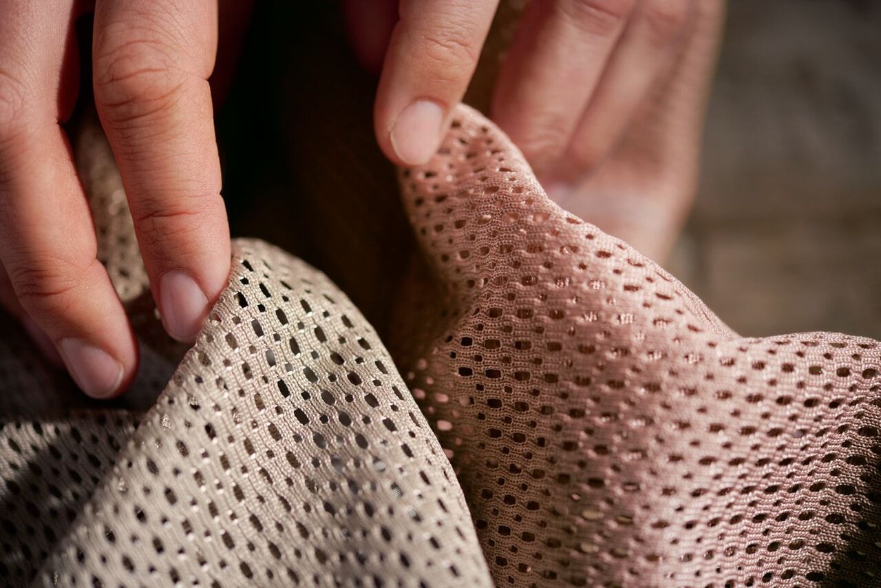 Close-up of hands touching two pieces of perforated fabric, one beige and one pink, highlighting texture and detail.