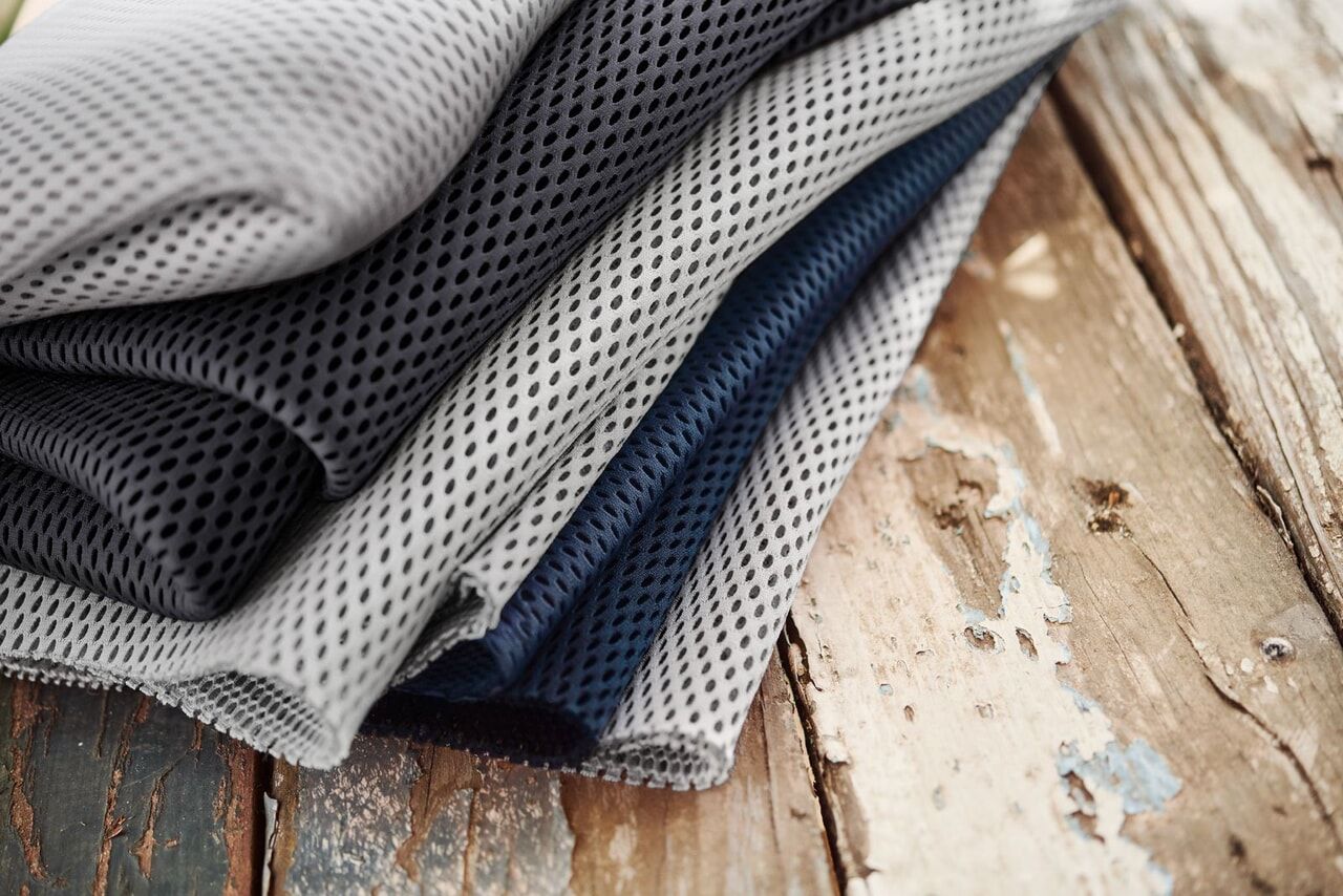 Folded mesh fabric in gray and navy blue, laid on a rustic wooden surface with peeling paint.
