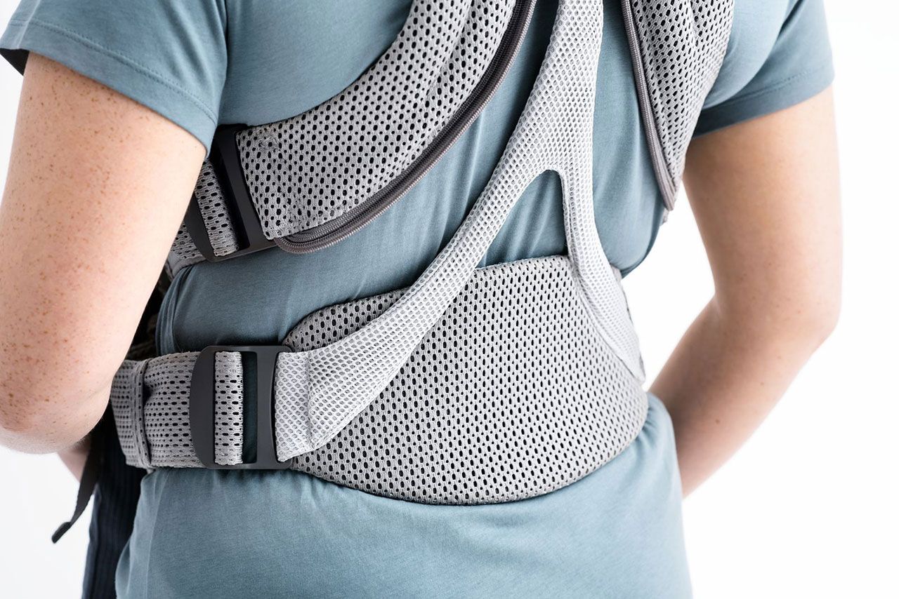 Person wearing a gray posture corrector over a teal shirt, showing the back view with adjustable straps and mesh padding.