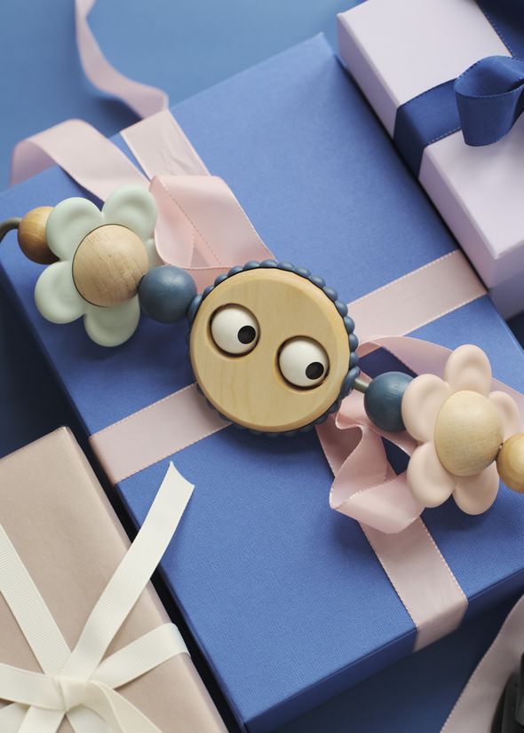 Colorful gift boxes with pink and blue ribbons, adorned with a playful wooden toy featuring eyes and flower shapes.