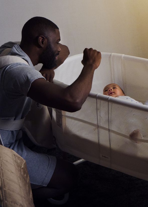 A man gently interacts with a smiling baby in a crib, creating a warm and nurturing atmosphere in a softly lit room.