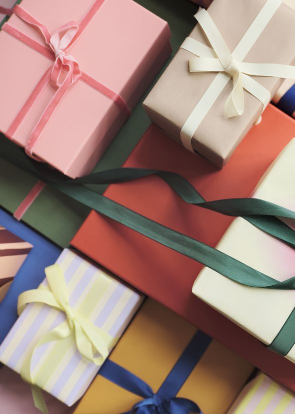 Colorful gift boxes with various ribbons arranged closely together, featuring pink, red, green, and striped patterns on a soft pink background.