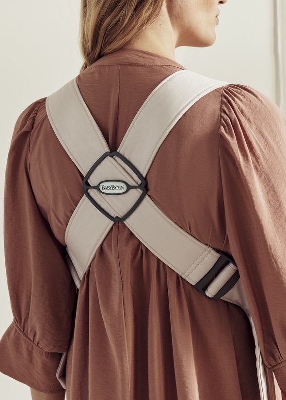 Back view of a person wearing a beige BabyBjörn baby carrier harness over a rust-colored dress.
