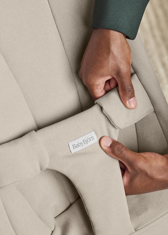 Hands adjusting the strap of a beige BabyBjörn baby seat.