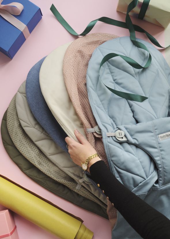 A person arranges a variety of colorful fabric swatches on a pink surface, surrounded by wrapped gifts and decorative ribbons.