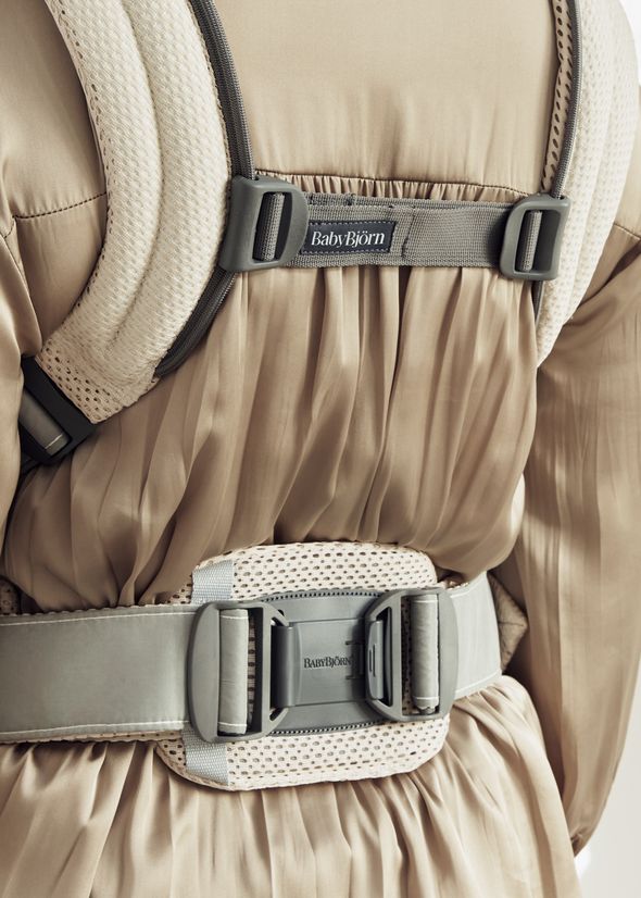 Close-up of a person wearing a beige dress and a gray BabyBjörn carrier, showing detailed buckle and strap design.