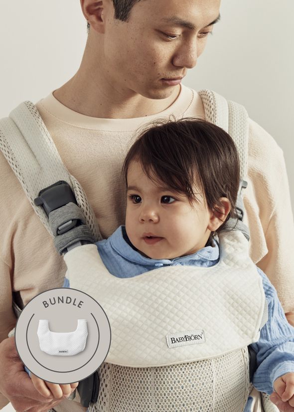 A person carrying a baby in a white BabyBjörn carrier. The baby is wearing a blue shirt. A "bundle" label is displayed on the image.