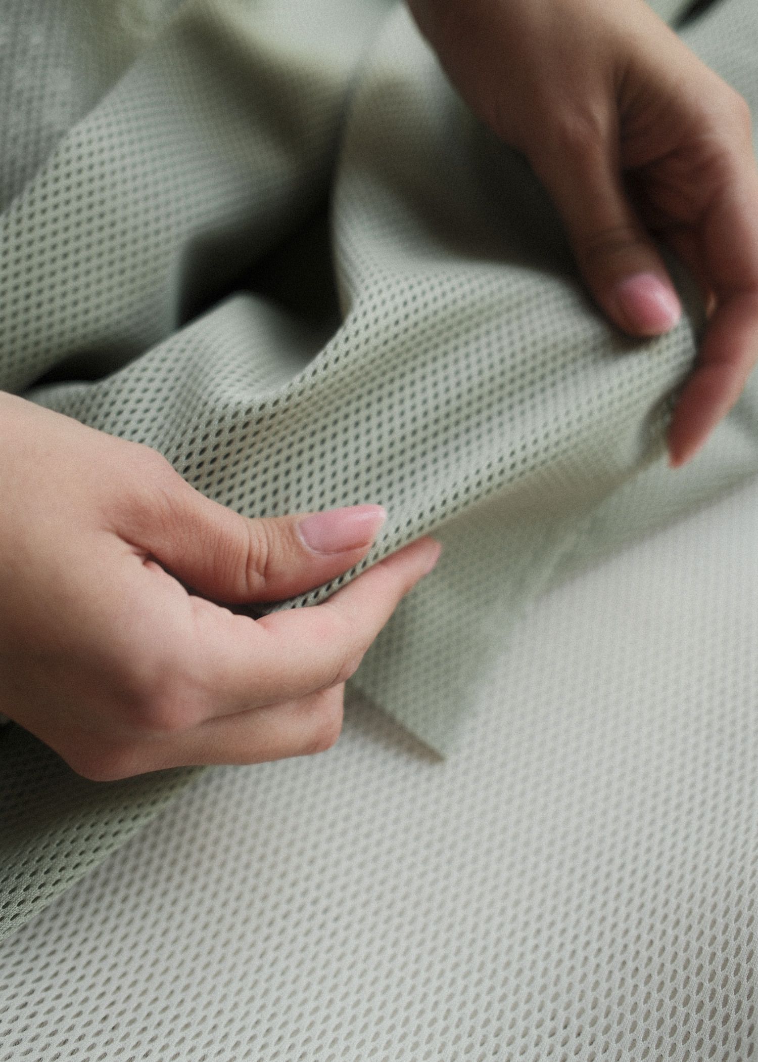 Hands holding and feeling a piece of light green, textured mesh fabric.